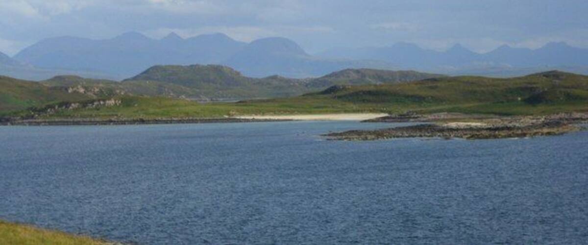 A coastal landscape with a body of water, grassy hills, and distant mountains.