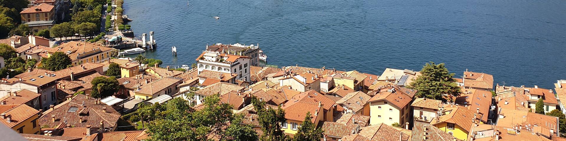 A coastal town with terracotta-roofed buildings, a marina, and a backdrop of mountains.