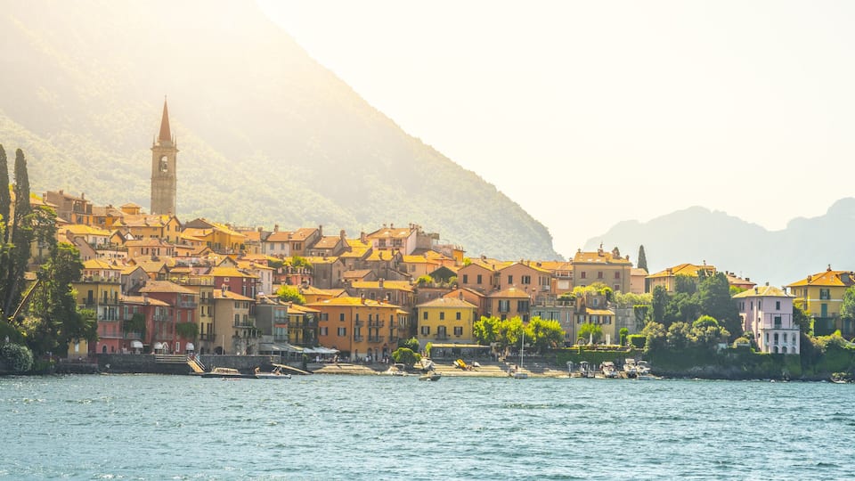 A coastal town with colorful buildings, a prominent church tower, and a mountain in the background.