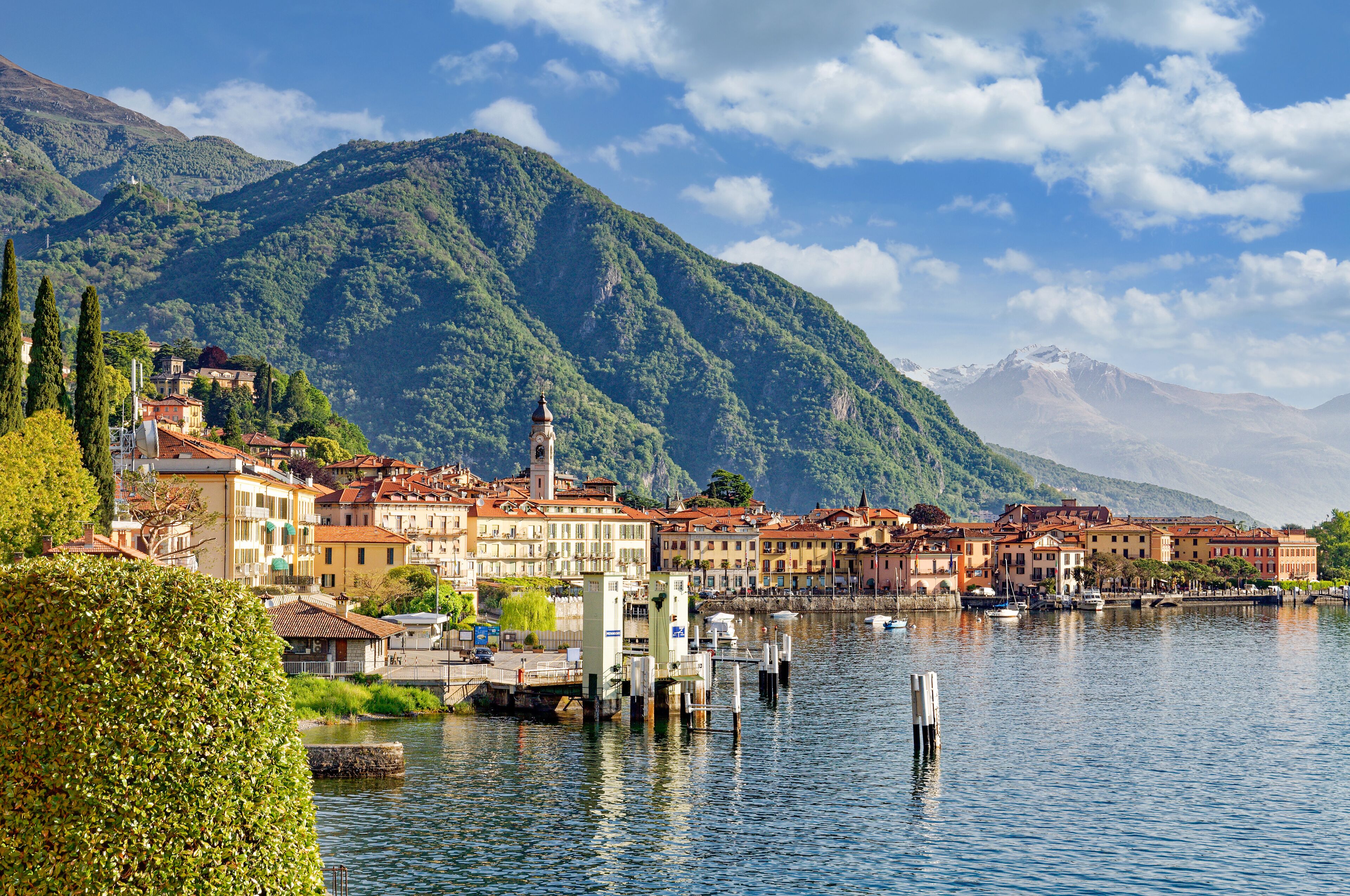 A lakeside town with historic buildings, a prominent church tower, and mountains in the background.