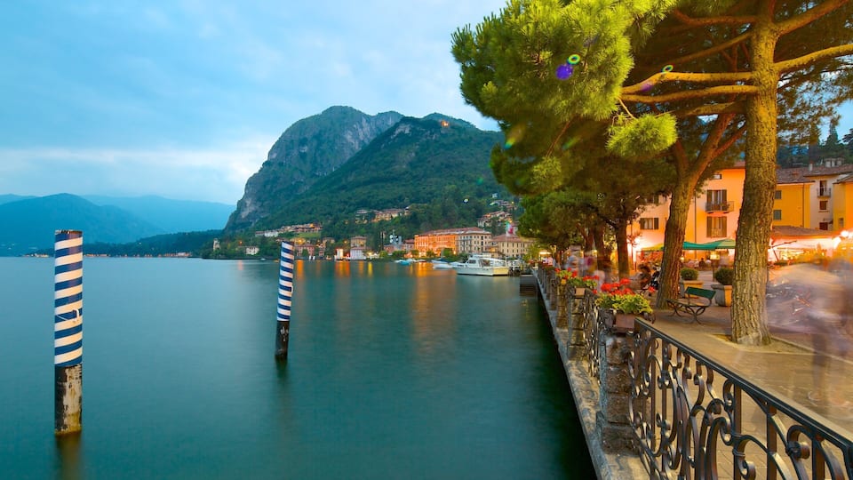 A calm lake with boats, a mountain in the background, and buildings along the shore.
