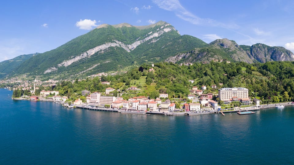 A coastal town with a mountain backdrop, a harbor with boats, and lush greenery.