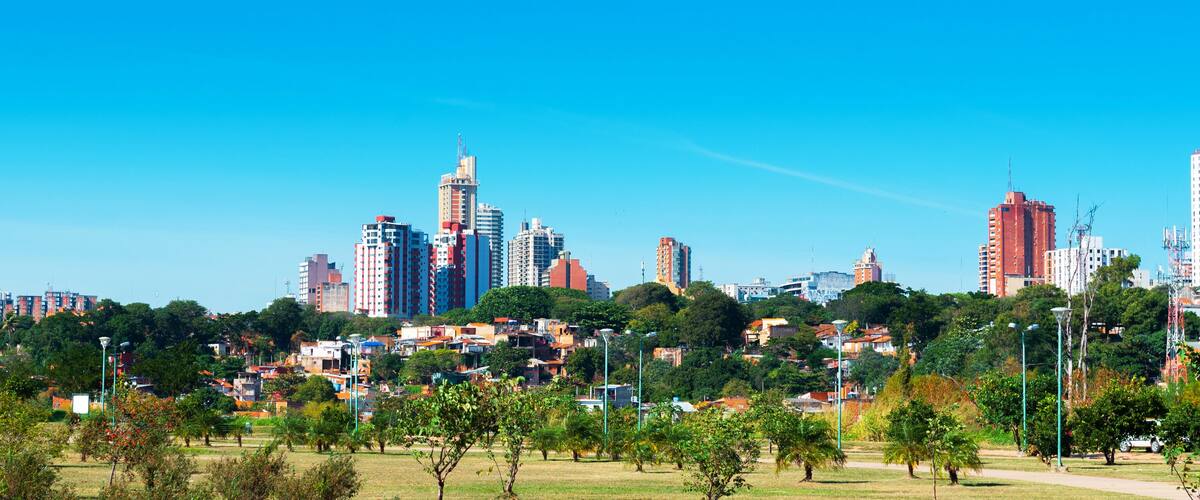A cityscape with high-rise buildings, a park with trees, and a clear blue sky.