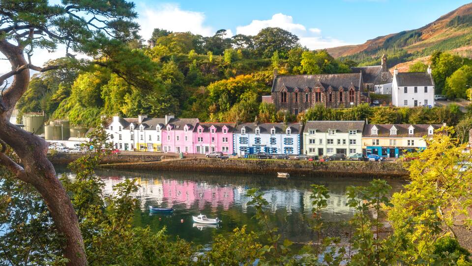 A picturesque riverside town with colorful buildings, a boat on the water, and lush greenery.