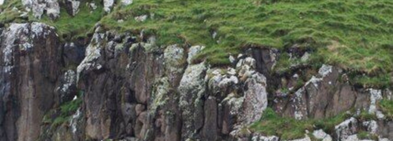 Una estructura de piedra en ruinas sobre un acantilado cubierto de hierba.