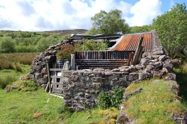 A stone structure with a tiled roof, surrounded by greenery and hills.