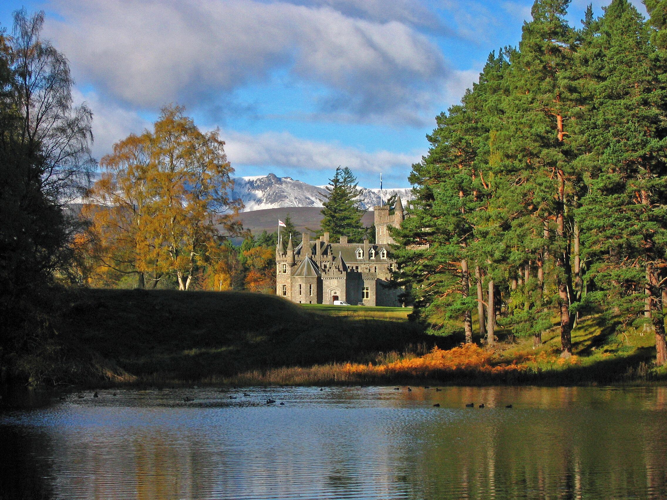 A castle surrounded by autumn trees and a lake.
