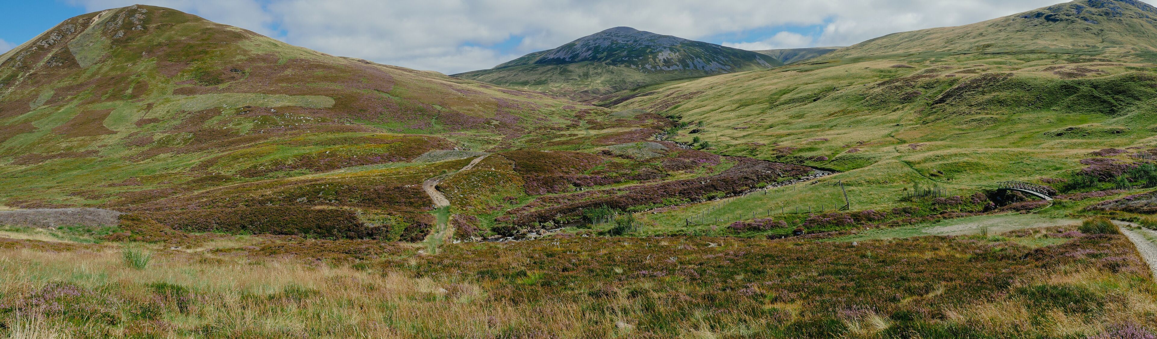 A mountainous landscape with a winding path, a small stream, and a bridge.