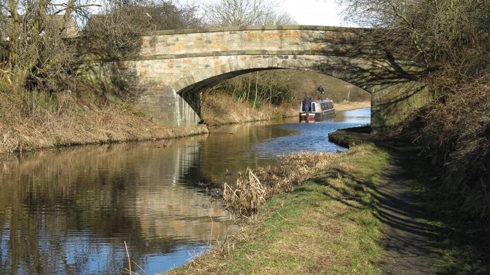 A stone bridge over a narrow canal with a boat and a person standing on it.