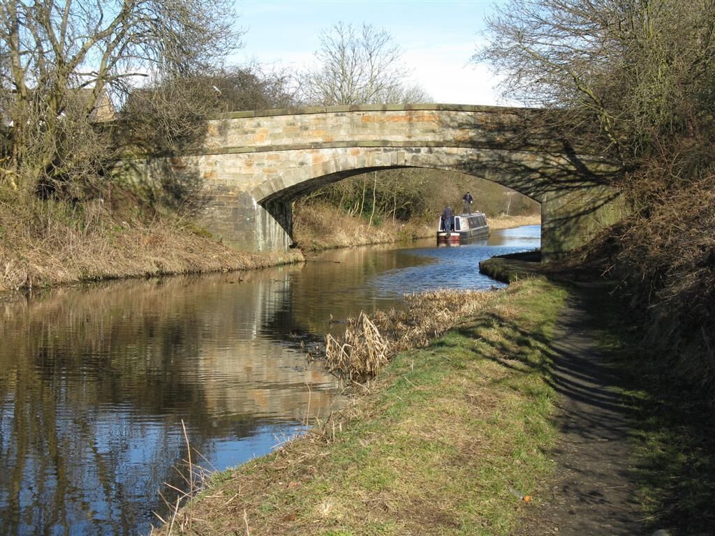 A stone bridge over a narrow canal with a boat and a person standing on it.