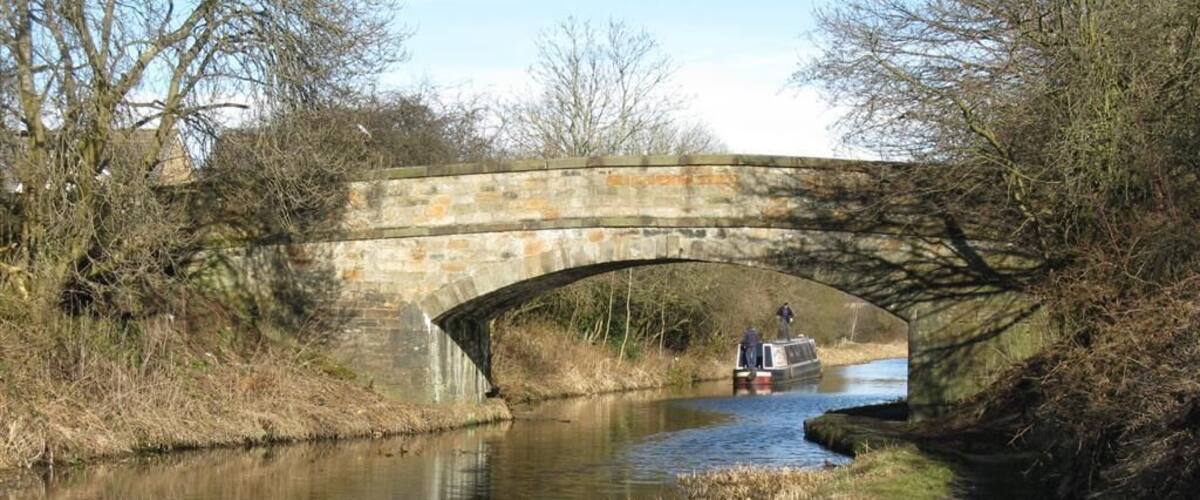A stone bridge over a narrow canal with a boat and a person standing on it.