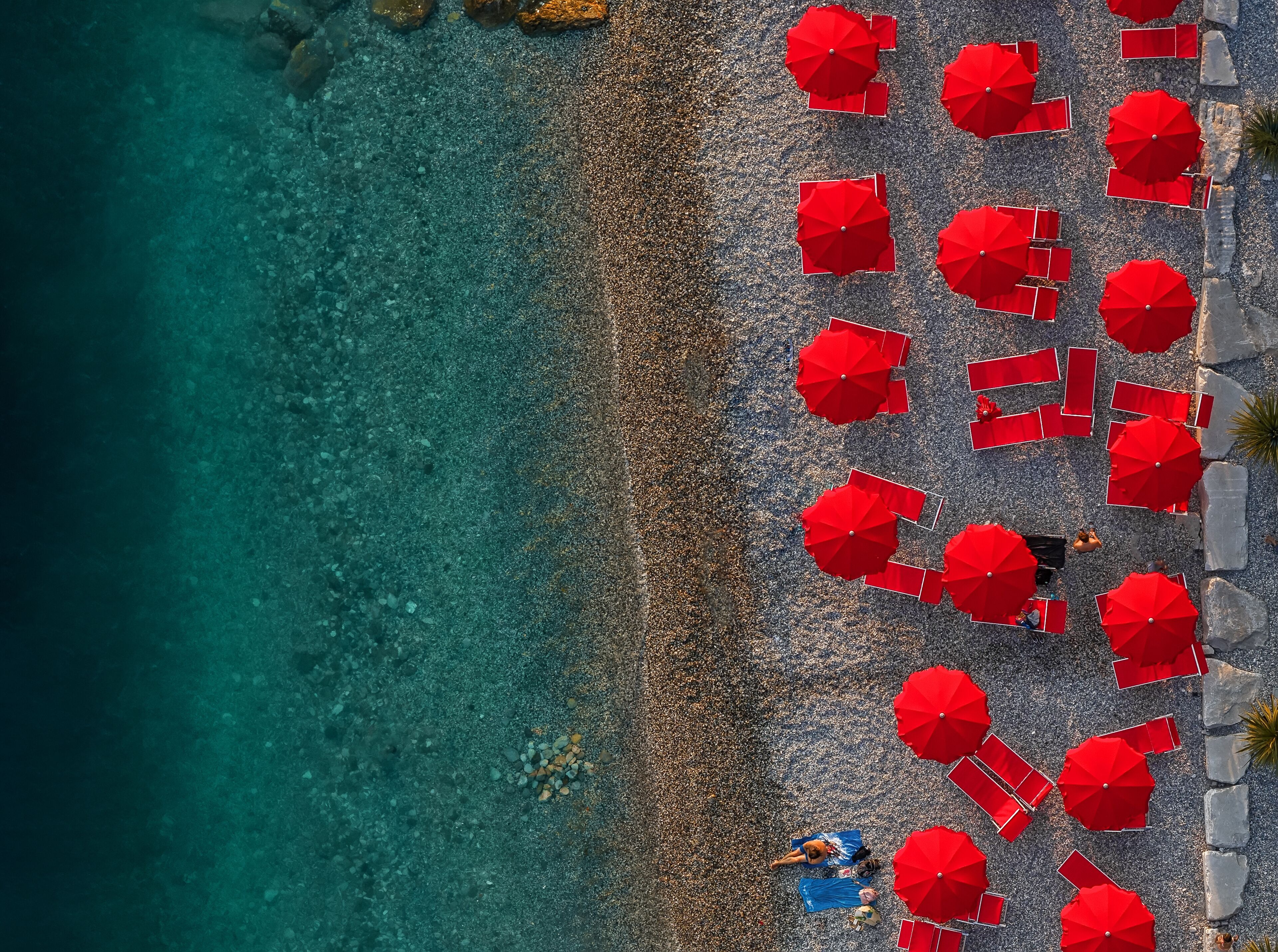 An aerial view of a beach with red umbrellas and clear turquoise water.