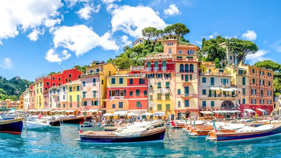 A colorful waterfront with boats docked and a hillside of Mediterranean-style buildings.