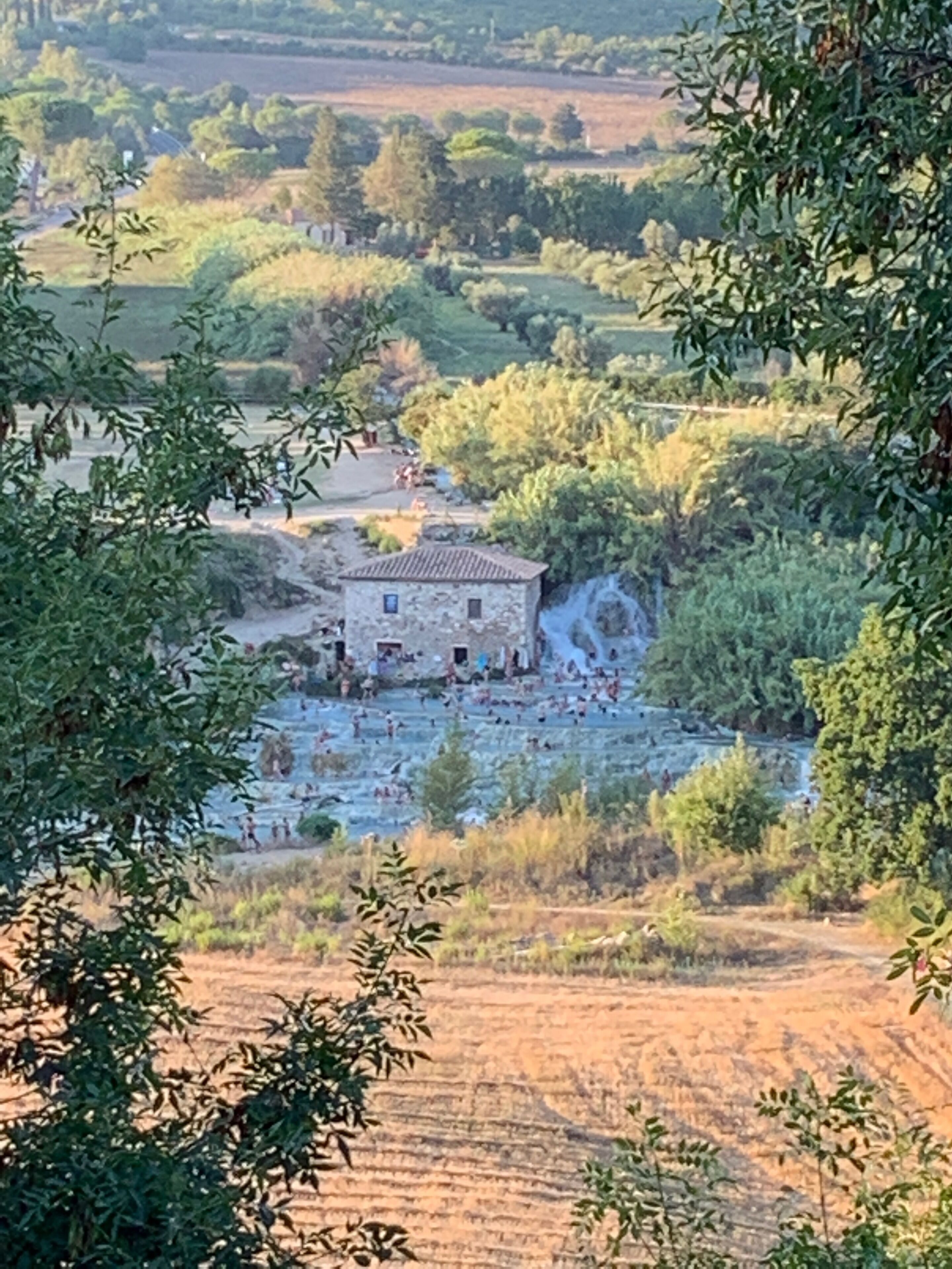A rural landscape with a stone building surrounded by trees and fields.