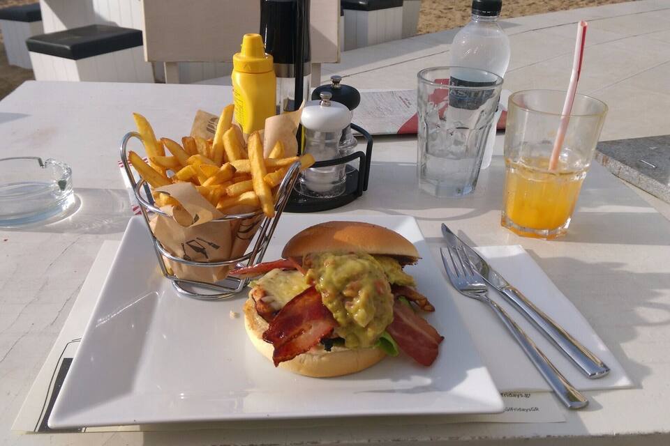 Uma refeição com hambúrguer, batatas fritas e uma bebida sobre a mesa.
