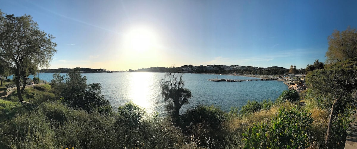 A lake with a pier, surrounded by trees and hills in the background.