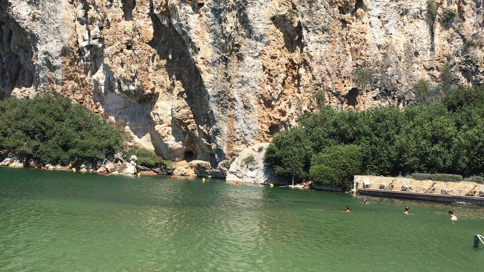 A rocky cliff with clear green water in front.