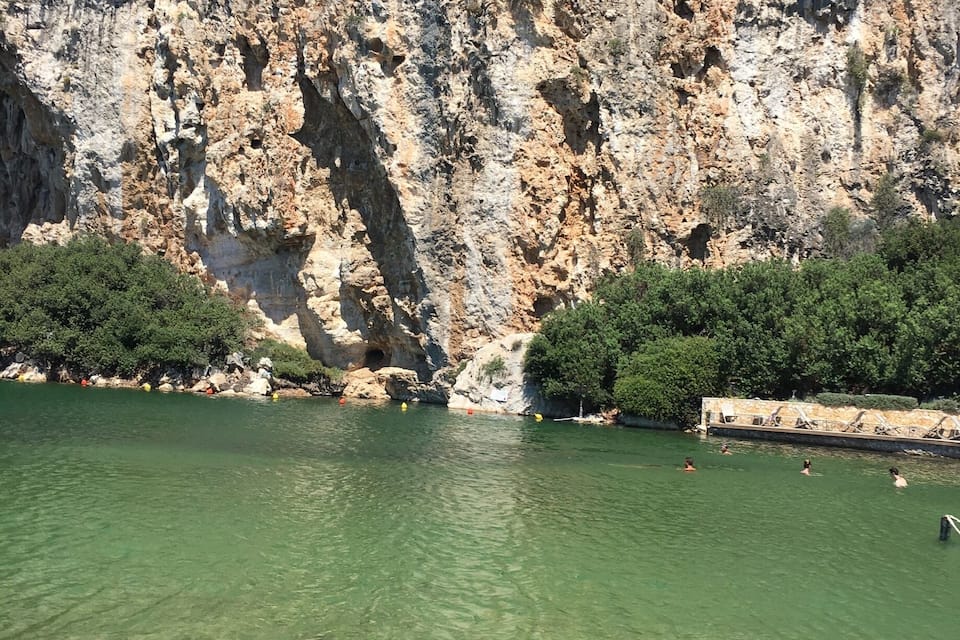 A rocky cliff with clear green water in front.