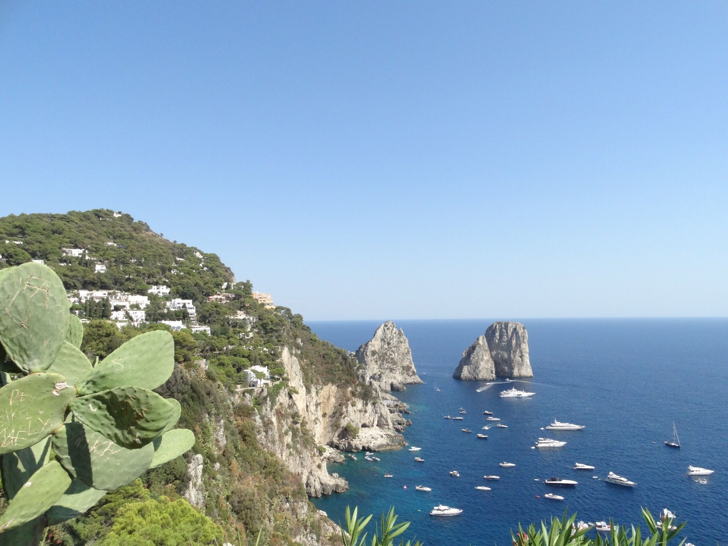 A coastal landscape with a cliff, houses, and boats.