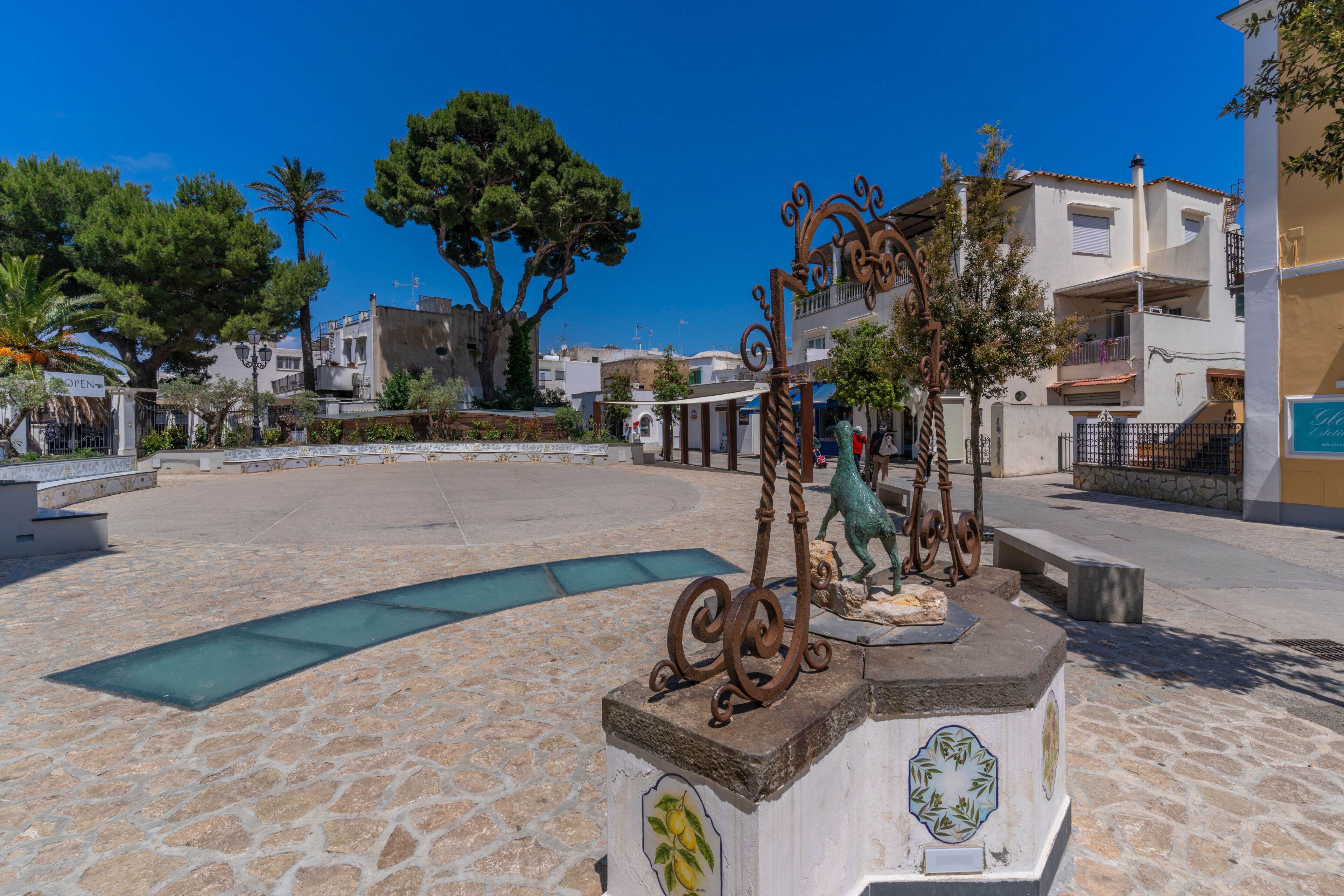 Una plaza con una fuente, baldosas de piedra y edificios al fondo.