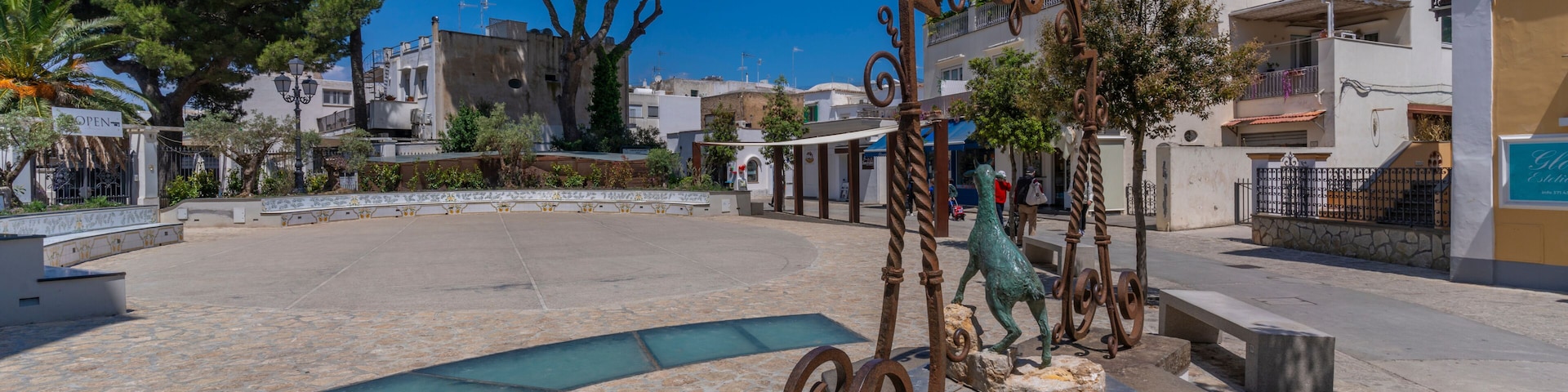 Una plaza con una fuente, baldosas de piedra y edificios al fondo.