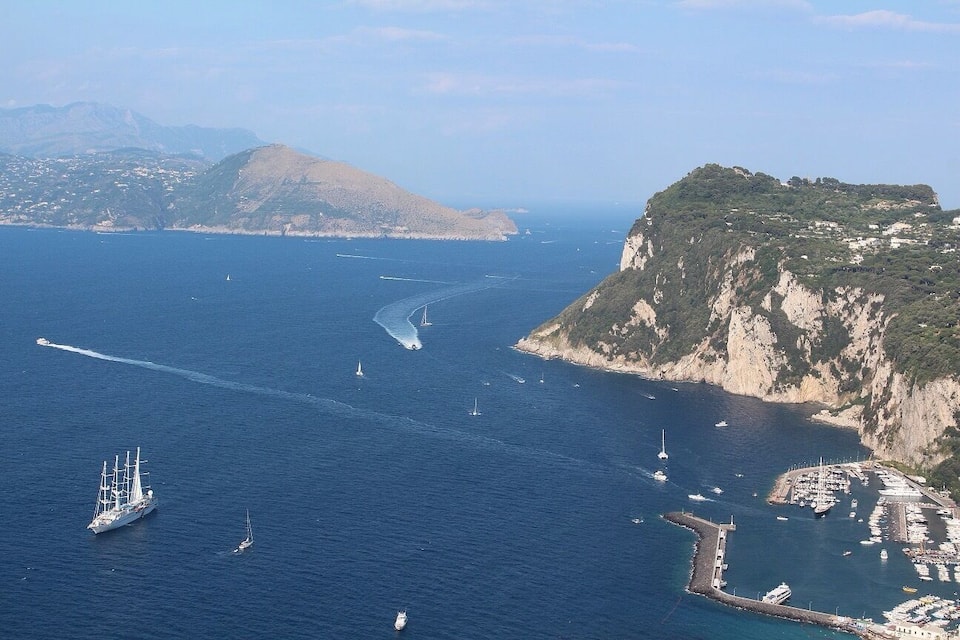 A coastal area with a large body of water, several sailboats, and a prominent cliff with a marina.