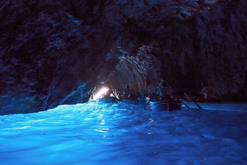 An ice cave with a blue glow and a small boat in the water.
