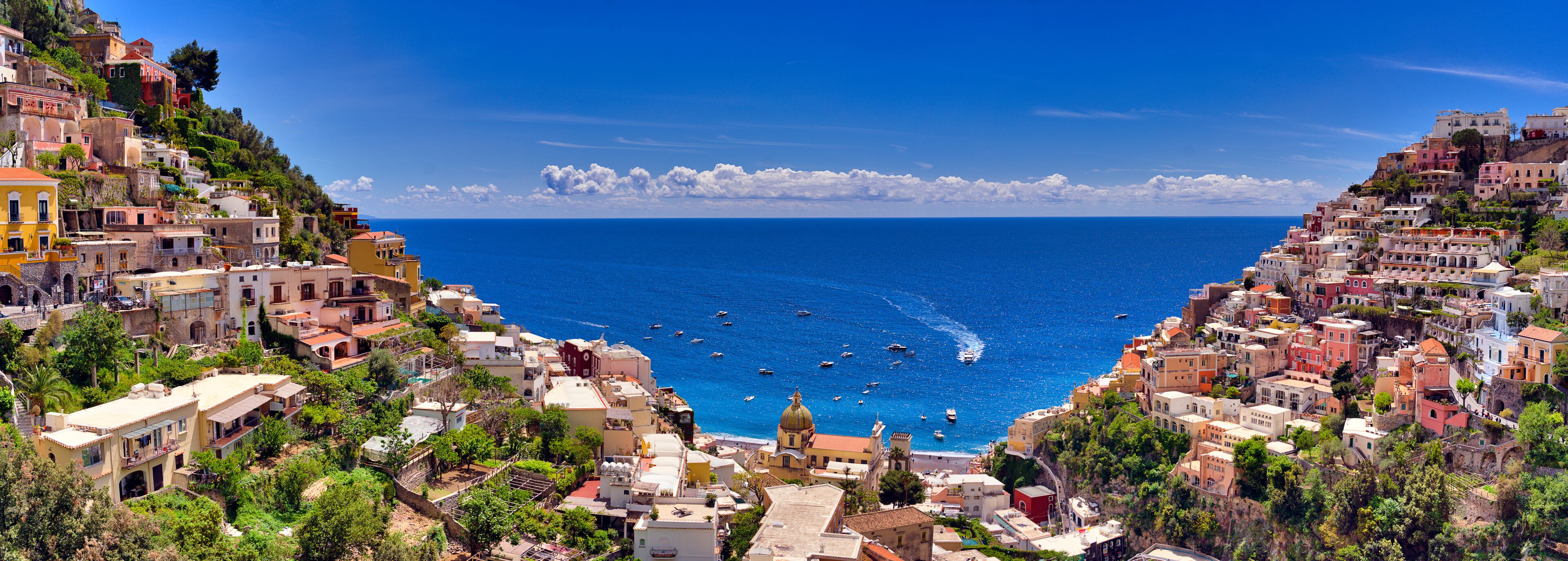 A coastal town with colorful buildings, a clear blue sea, and boats.