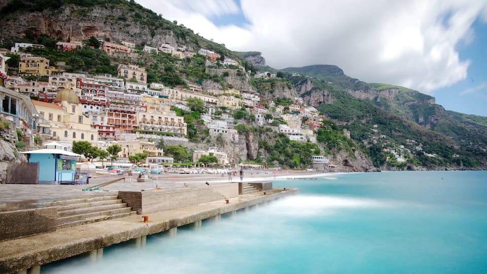 A coastal town with colorful buildings on a hillside, a calm sea, and a pier extending into the water.
