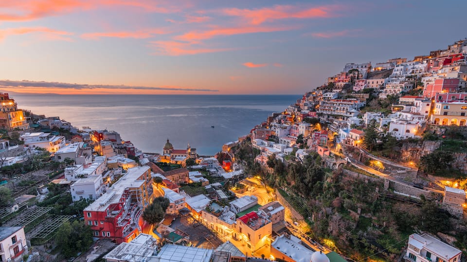 A coastal town at dusk with buildings along the hillside and a view of the sea.