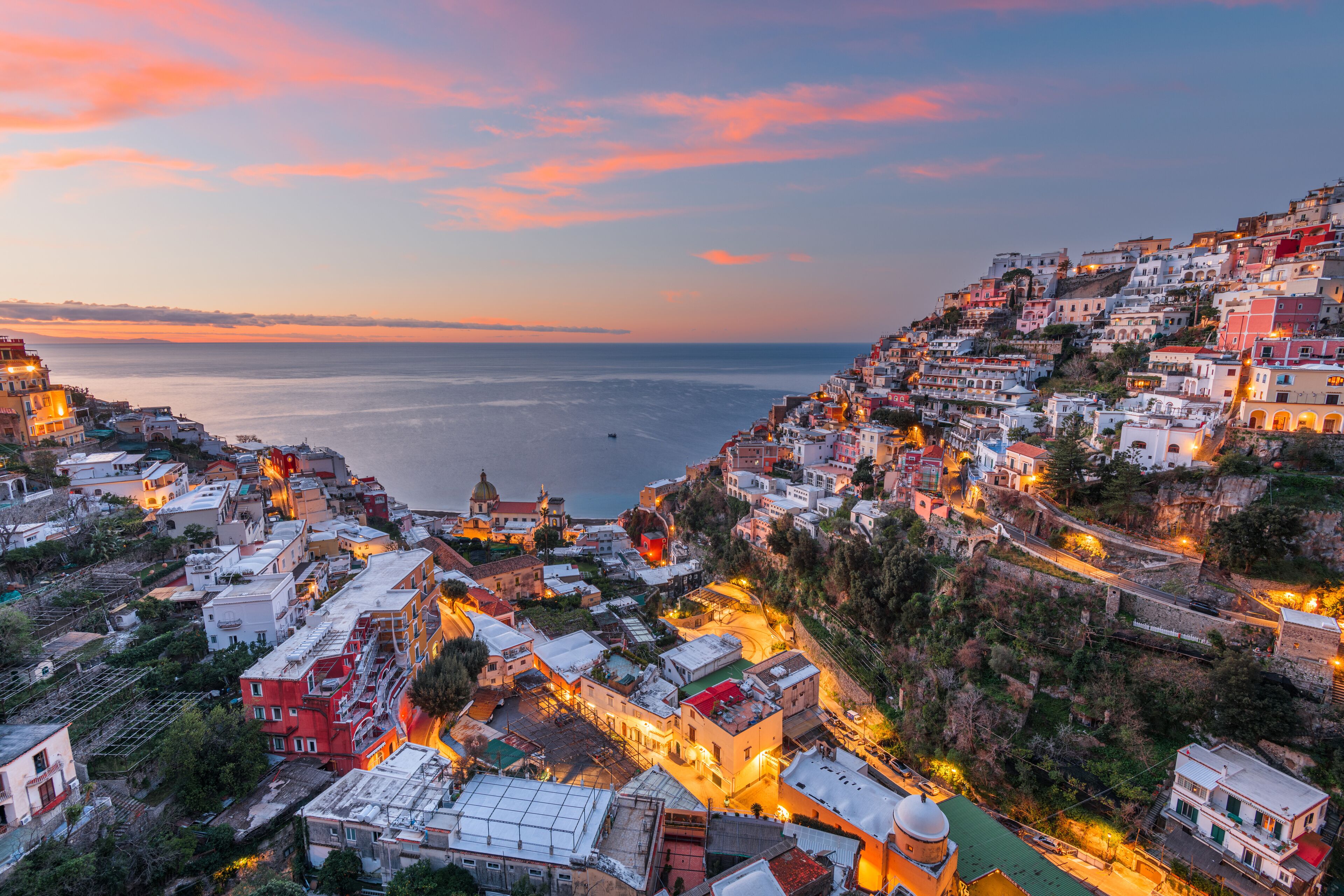 A coastal town at dusk with buildings along the hillside and a view of the sea.