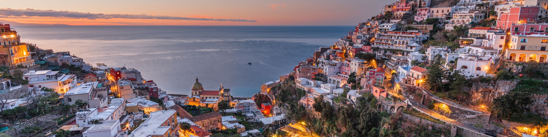 A coastal town at dusk with buildings along the hillside and a view of the sea.