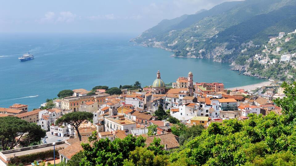 A coastal town with a prominent church dome, terraced houses, and a ship in the sea.