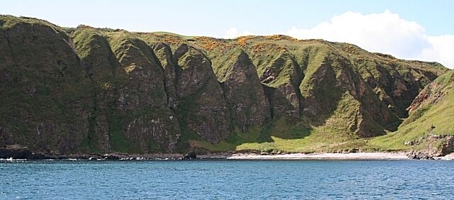 A coastal landscape with green hills and a beach.
