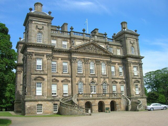 A large, historic stone building with a grand staircase, multiple windows, and a flag on top.