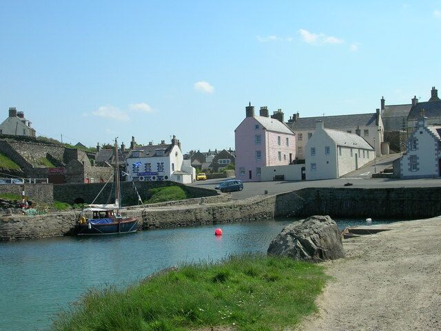 A coastal town with a harbor, a sailboat, and buildings along the shore.