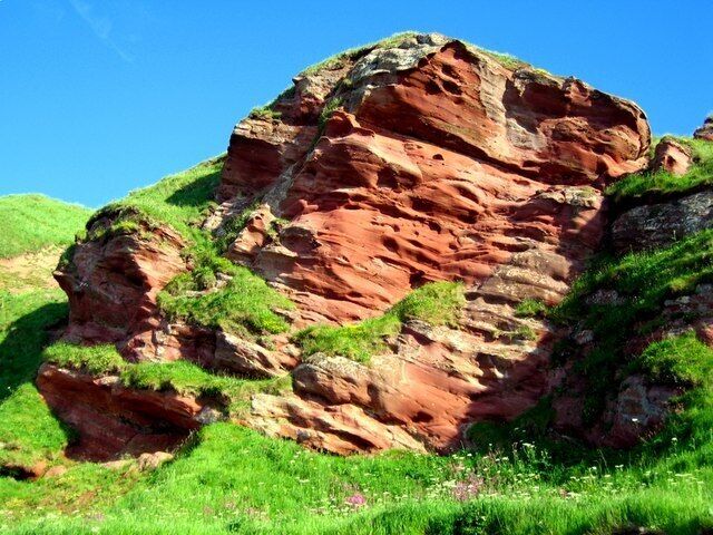 A large red rock formation with green grass around it.