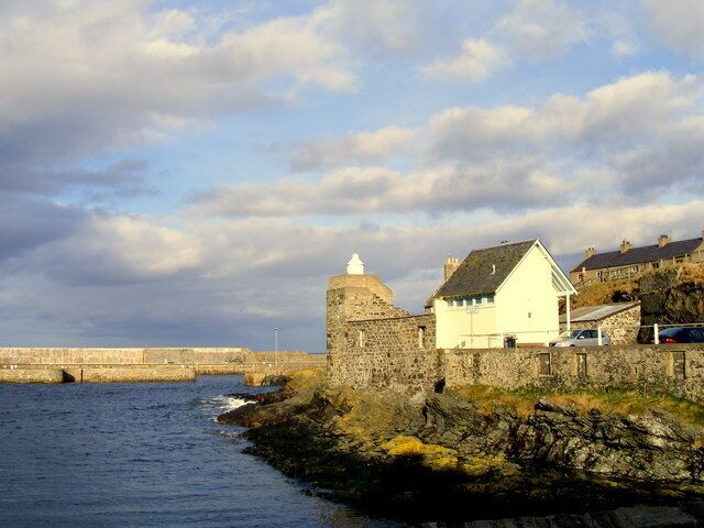 A coastal town with a stone fortification, a white building, and a bridge over the water.
