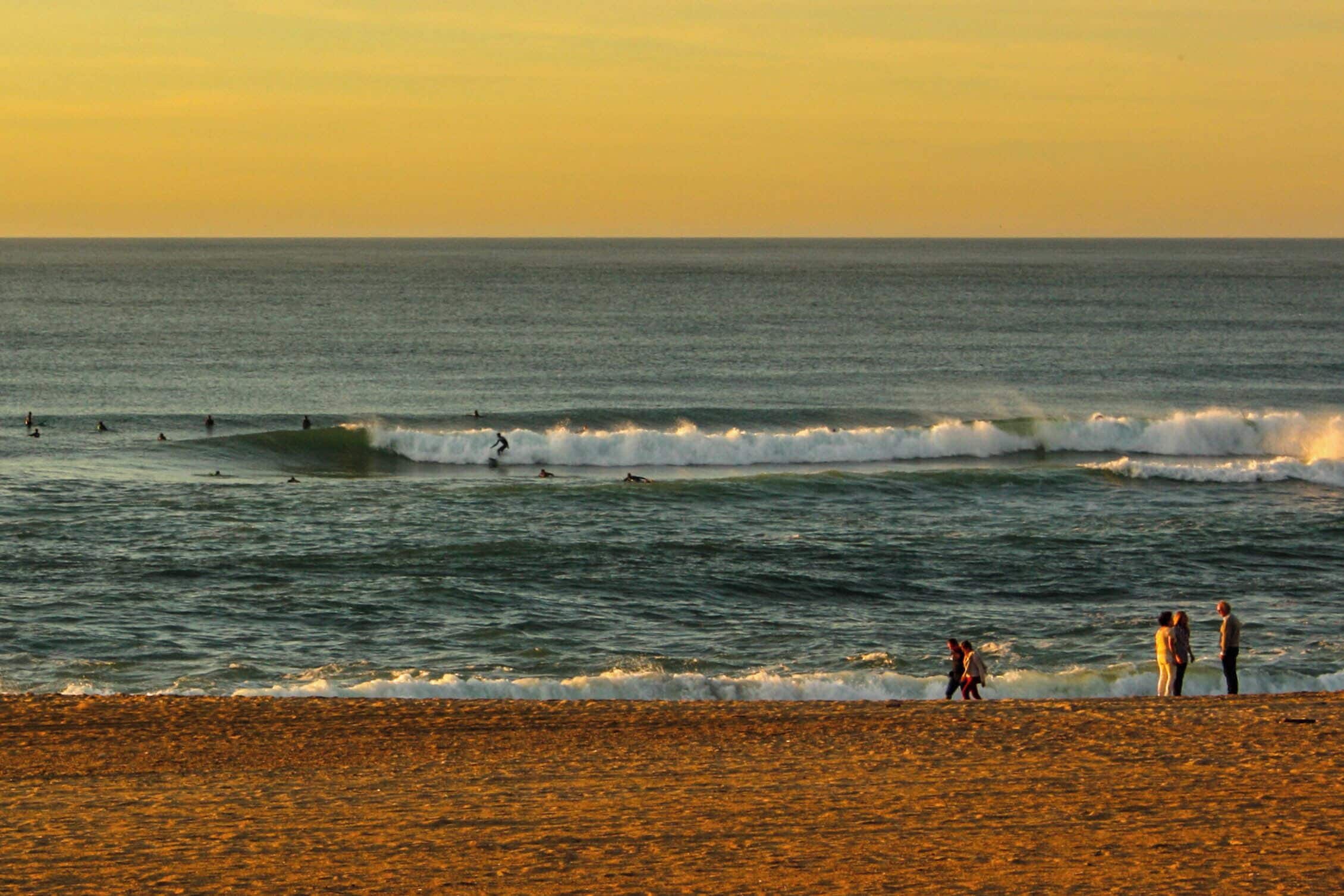 A beach with waves and people in the water.