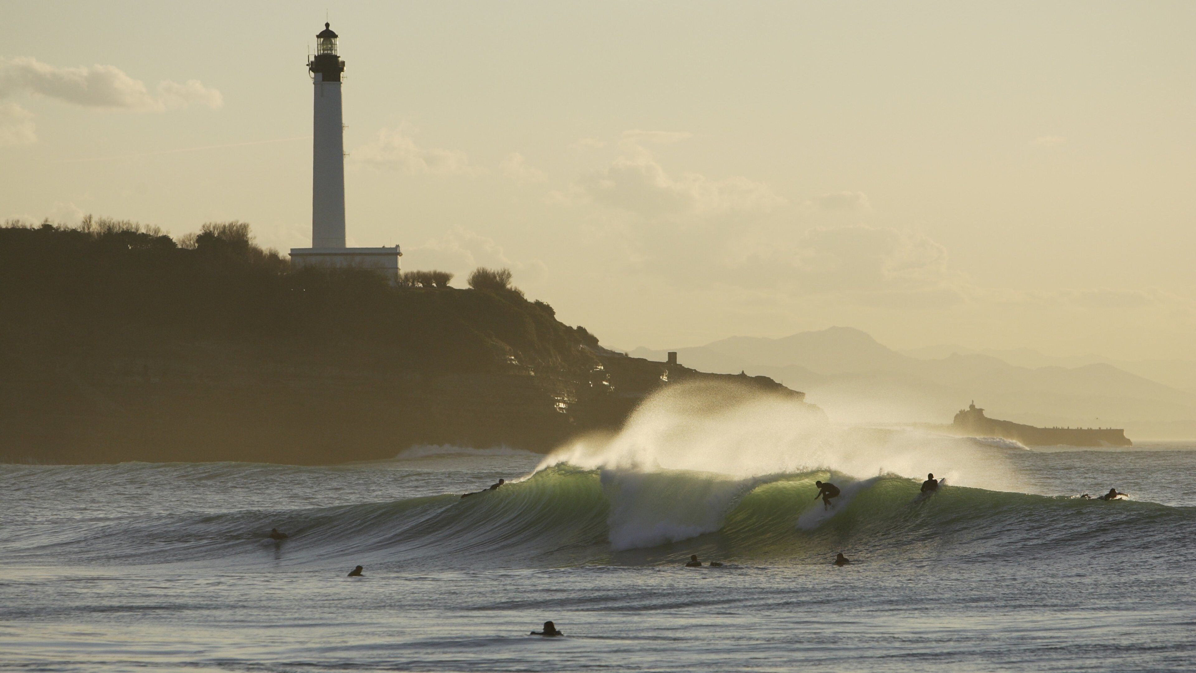A lighthouse, waves, and surfers.