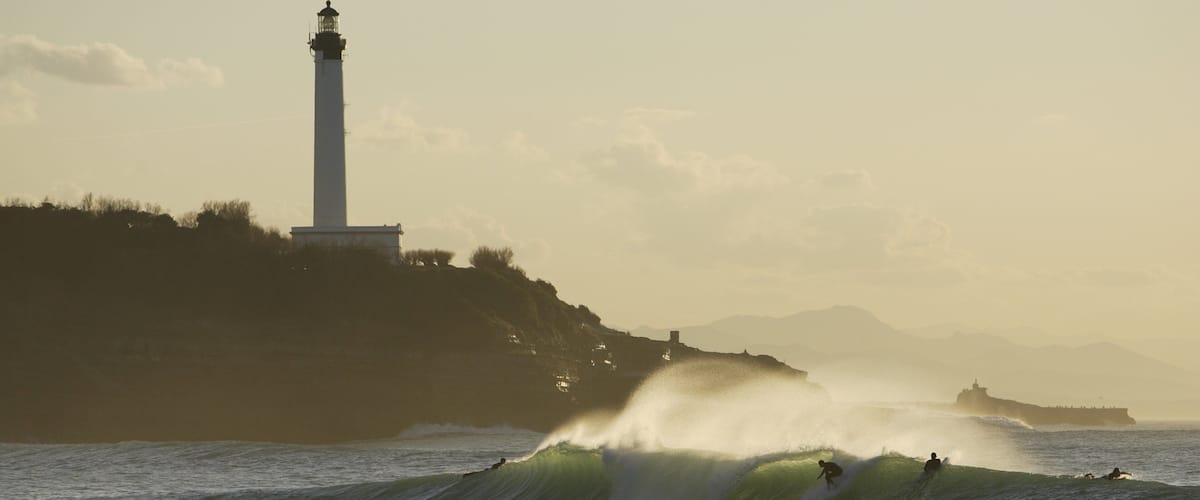 A lighthouse, waves, and surfers.