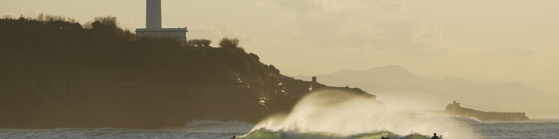 A lighthouse, waves, and surfers.