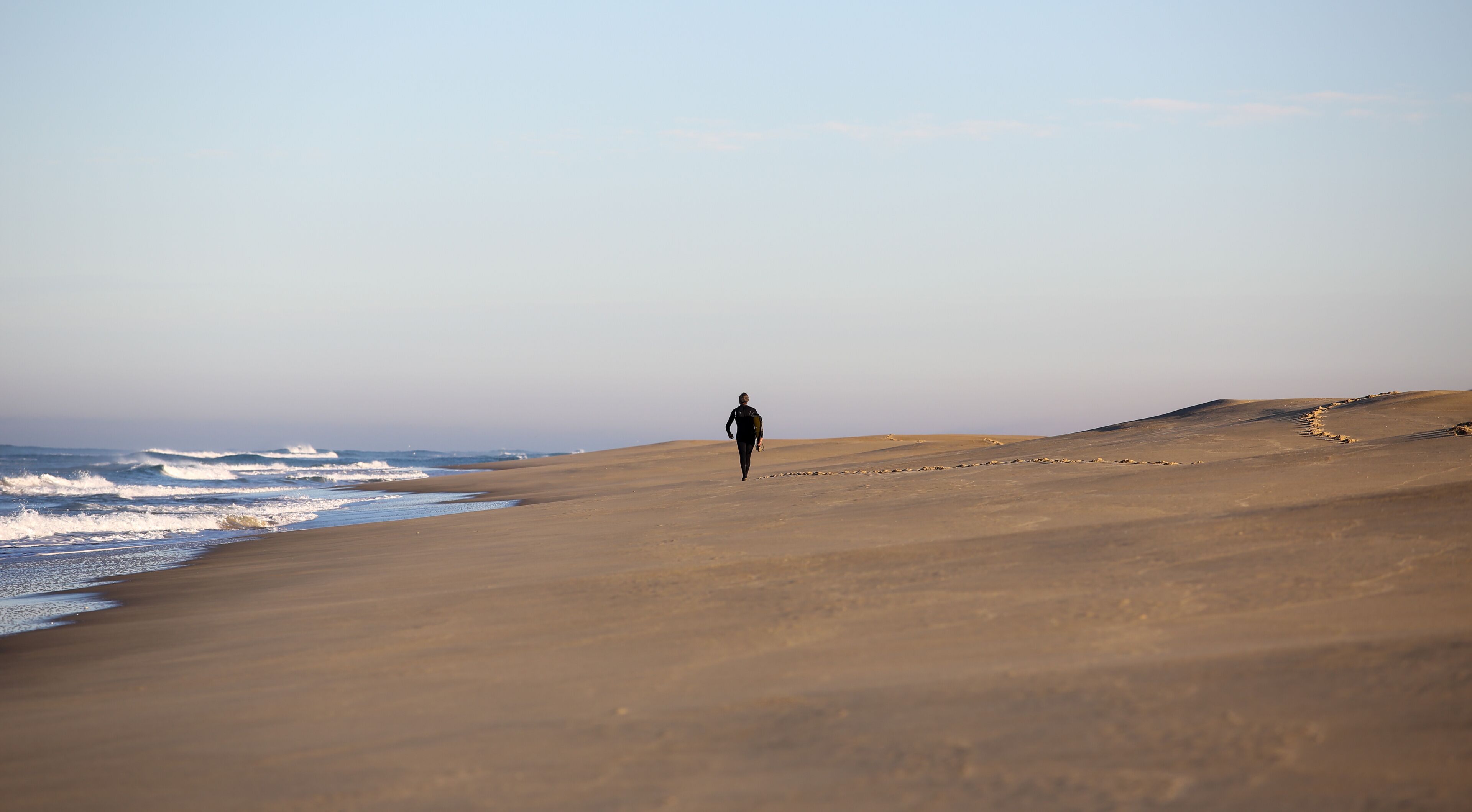A person walking on a sandy beach with waves in the background.