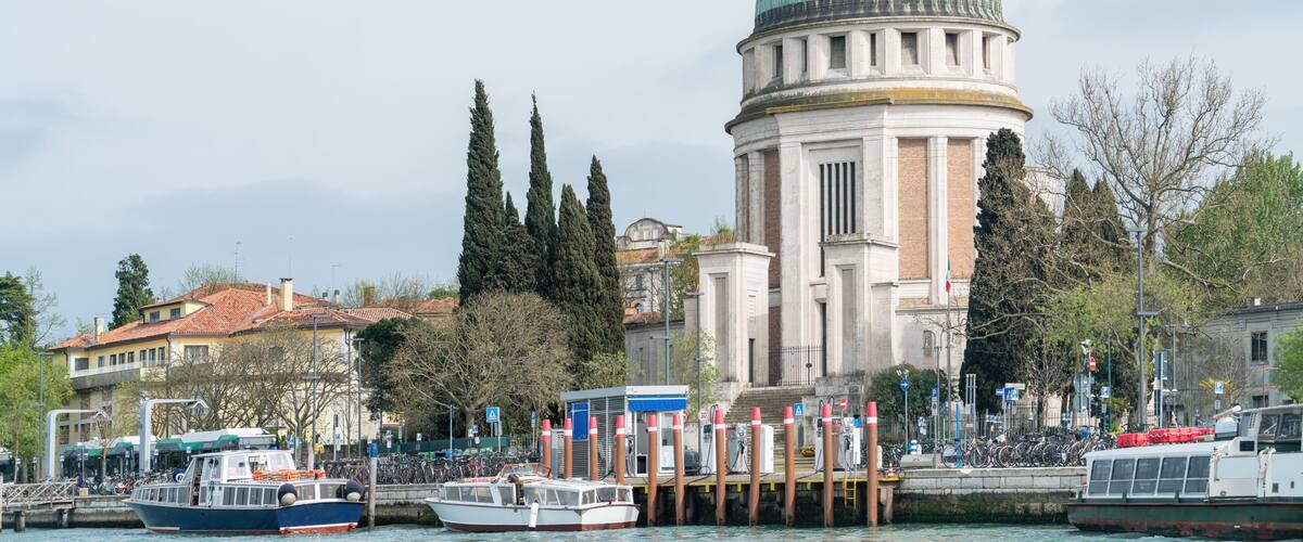 Waterfront view with boats and pier facing the Tempie Votivo di Santa Maria Immacolata with green dome on Lido di Venezia near Venice Italy