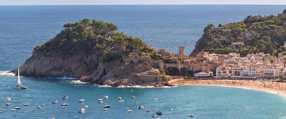 Aerial view of boats in bay with historic castle and rocky coastline in Tossa de Mar on sunny day, Spain, Catalonia