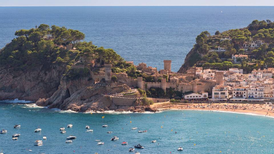 Aerial view of boats in bay with historic castle and rocky coastline in Tossa de Mar on sunny day, Spain, Catalonia
