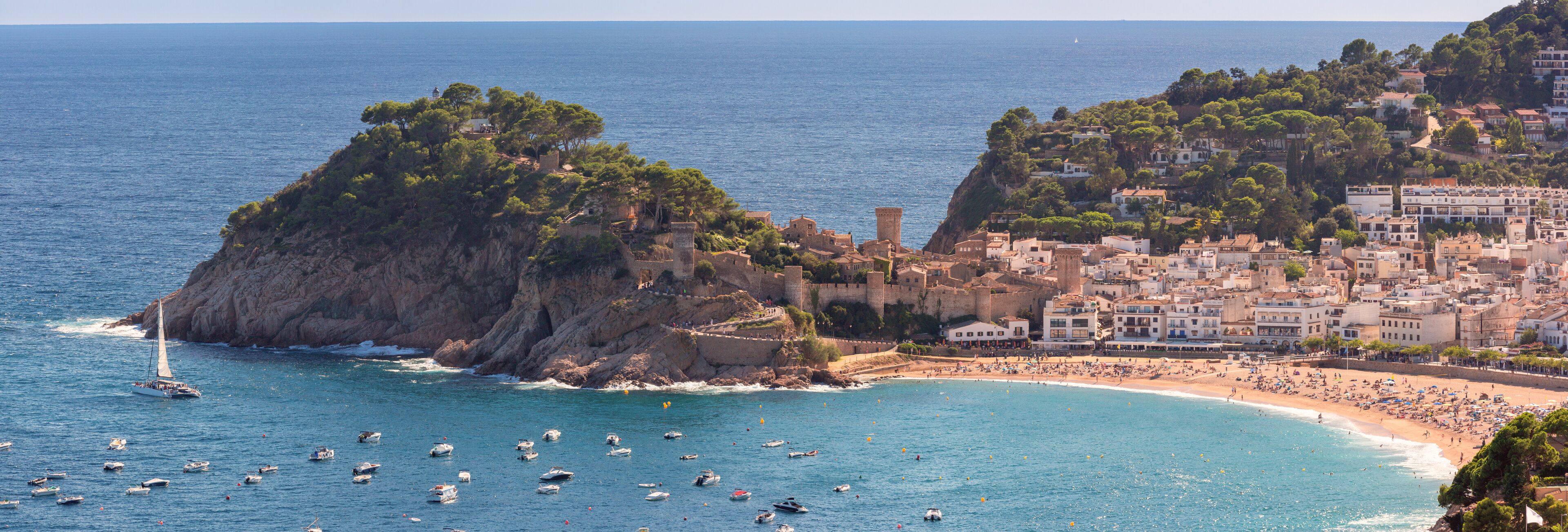 A coastal town with a prominent rocky island, a beach, and a historic castle.