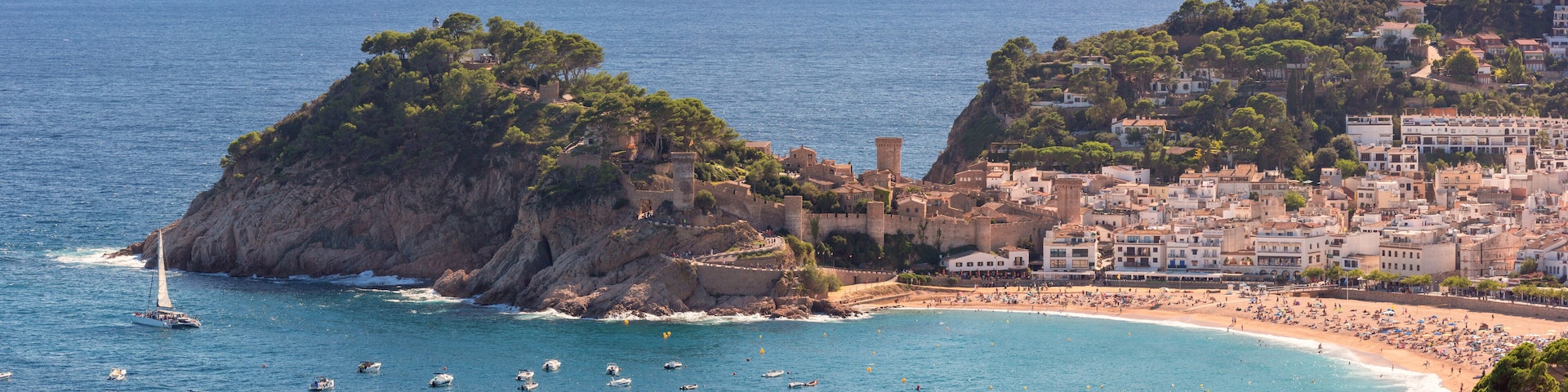 A coastal town with a prominent rocky island, a beach, and a historic castle.