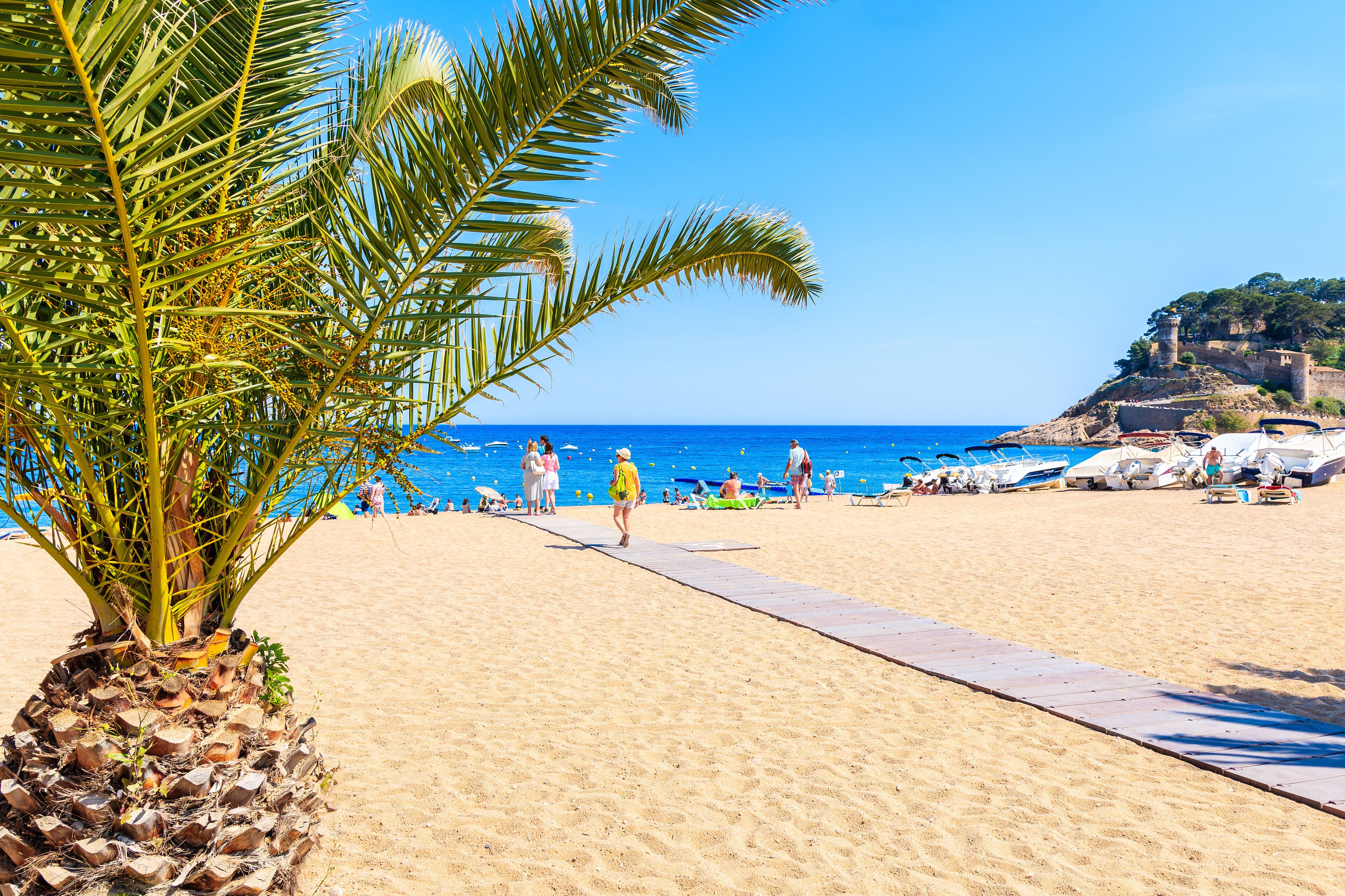 TOSSA DE MAR, SPAIN - JUN 3, 2019: People walking on sandy beach in Tossa de Mar town, Costa Brava, Spain.