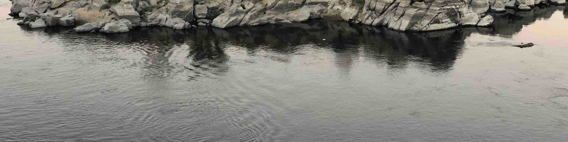 Um rio calmo com um afloramento rochoso no meio e um pequeno barco ancorado perto da margem.